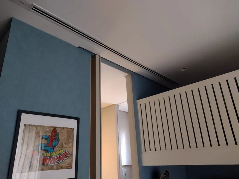 Long linear diffuser along a white ceiling above a blue wall, a sliding door and a slatted railing