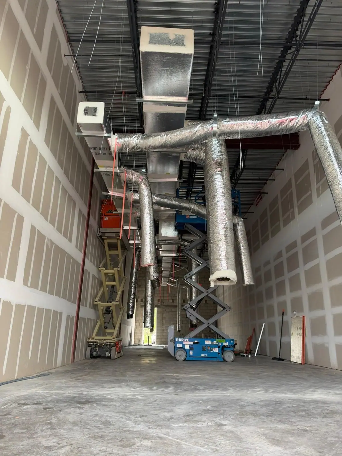 Interior under construction with ductwork hung from the ceiling beside scissor lifts