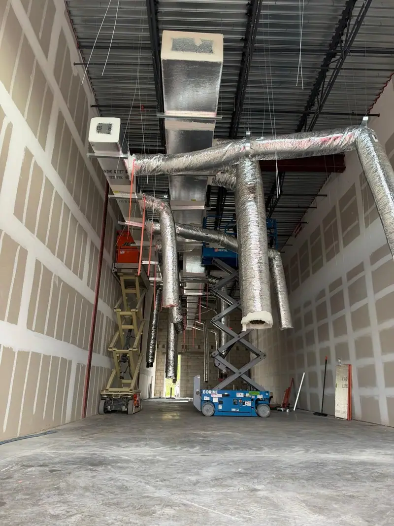 Interior under construction with ductwork hung from the ceiling beside scissor lifts